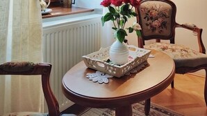 A cozy room with a round wooden table, a white vase with red flowers, a lamp, and a chair with floral upholstery. - La Teo Pensiune si Pivnita (Sighisoara)