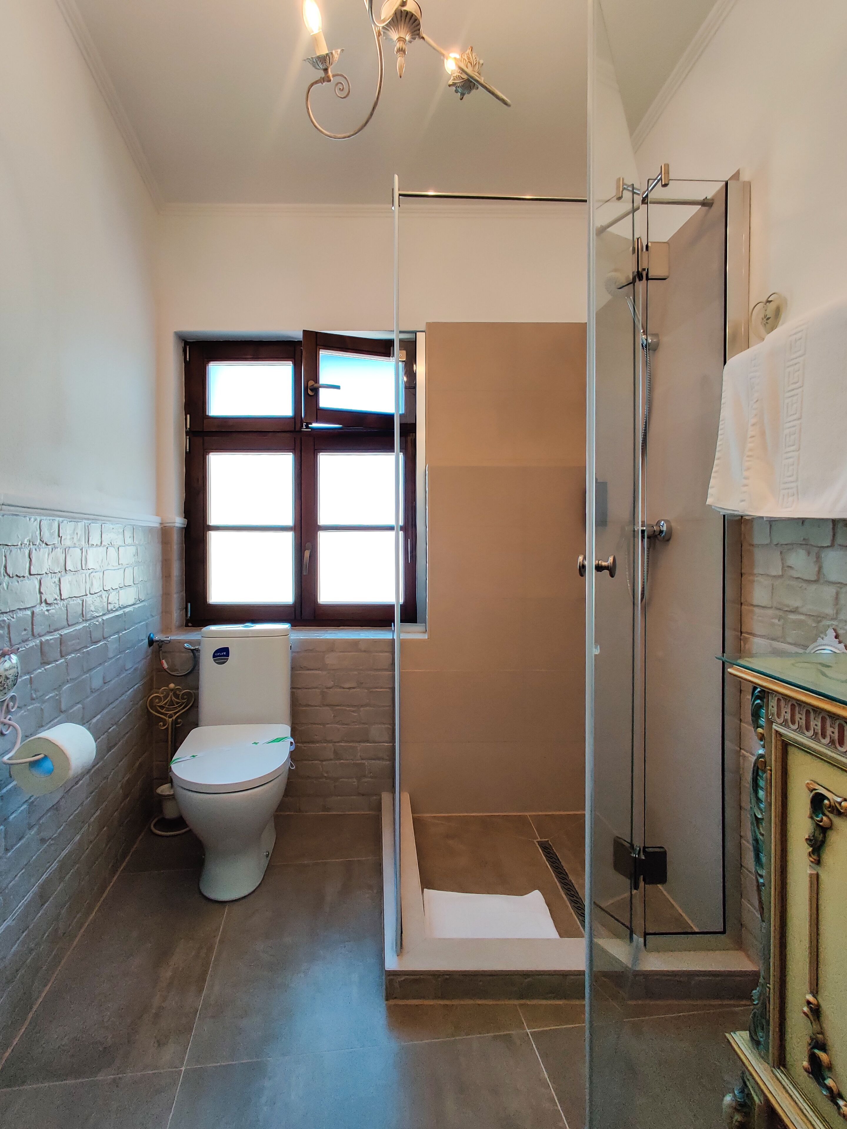 A bathroom with a toilet, a glass shower enclosure, and a window.