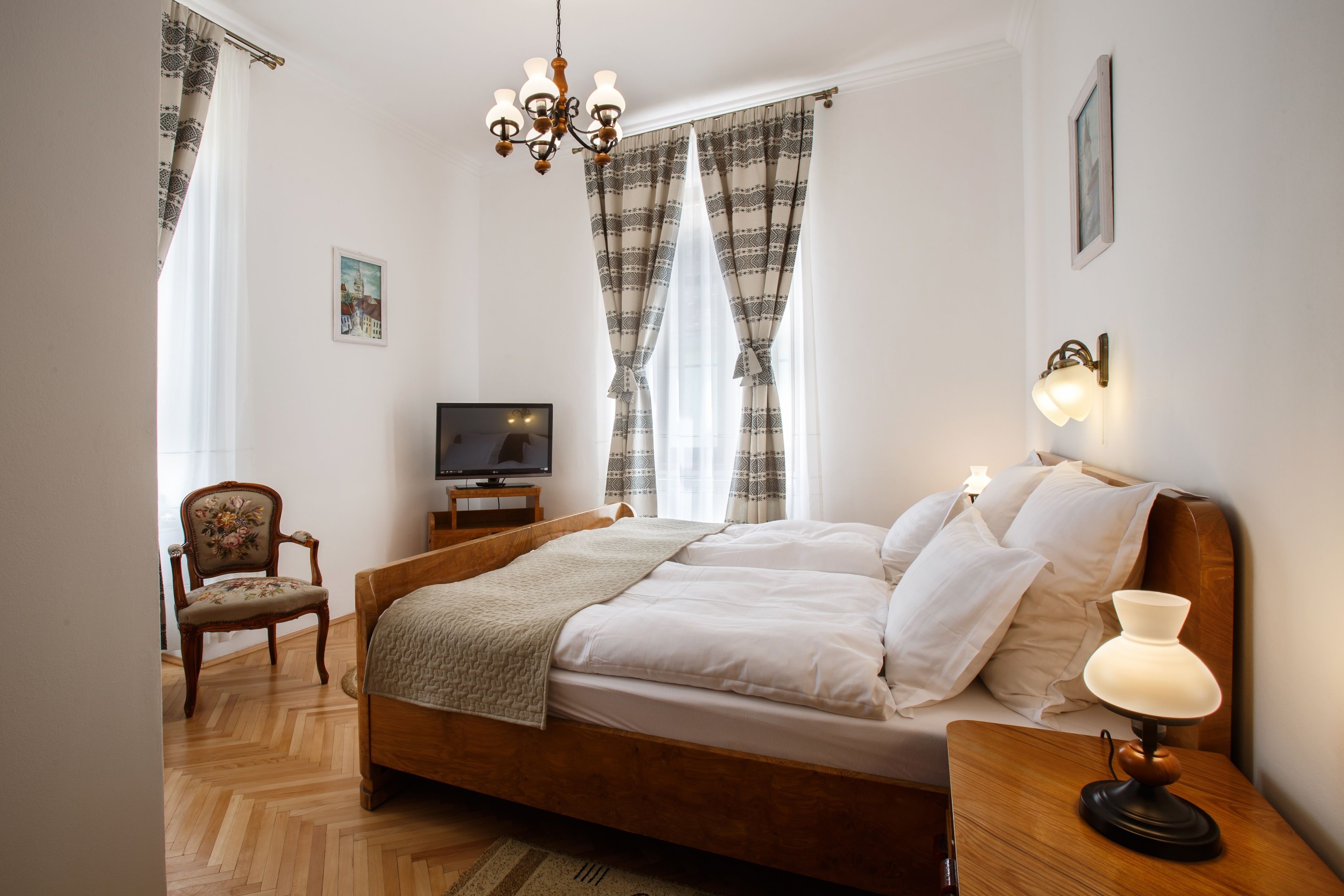 Een netjes opgemaakte slaapkamer met een houten bed, een stoel, een televisie en een bedlampje.