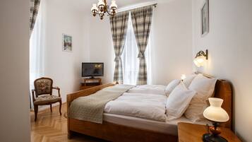 Een netjes opgemaakte slaapkamer met een houten bed, een stoel, een televisie en een bedlampje.