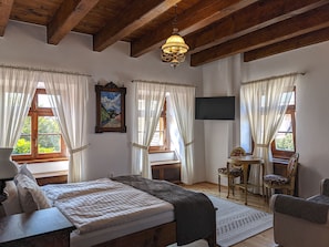 A bedroom with a bed, a desk, a chair, a TV, and a window with curtains.