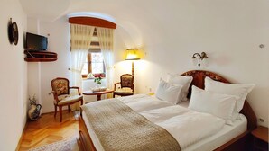A bedroom with a large bed, two chairs, a small table, a TV, and a window with curtains. - La Teo Pensiune si Pivnita (Sighisoara)
