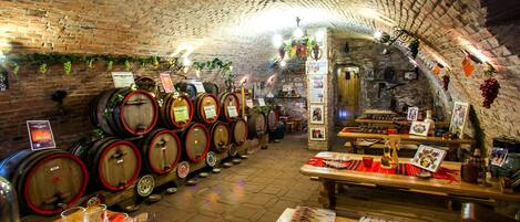 A wine cellar with wooden barrels, a dining area with tables and chairs, and a brick ceiling.