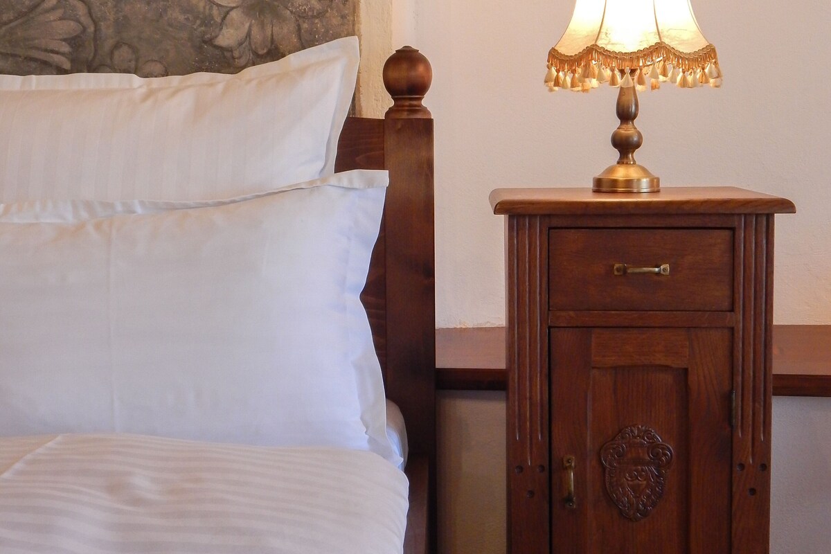 A neatly made bed with white linens, a wooden nightstand with a lamp, and a decorative wall.