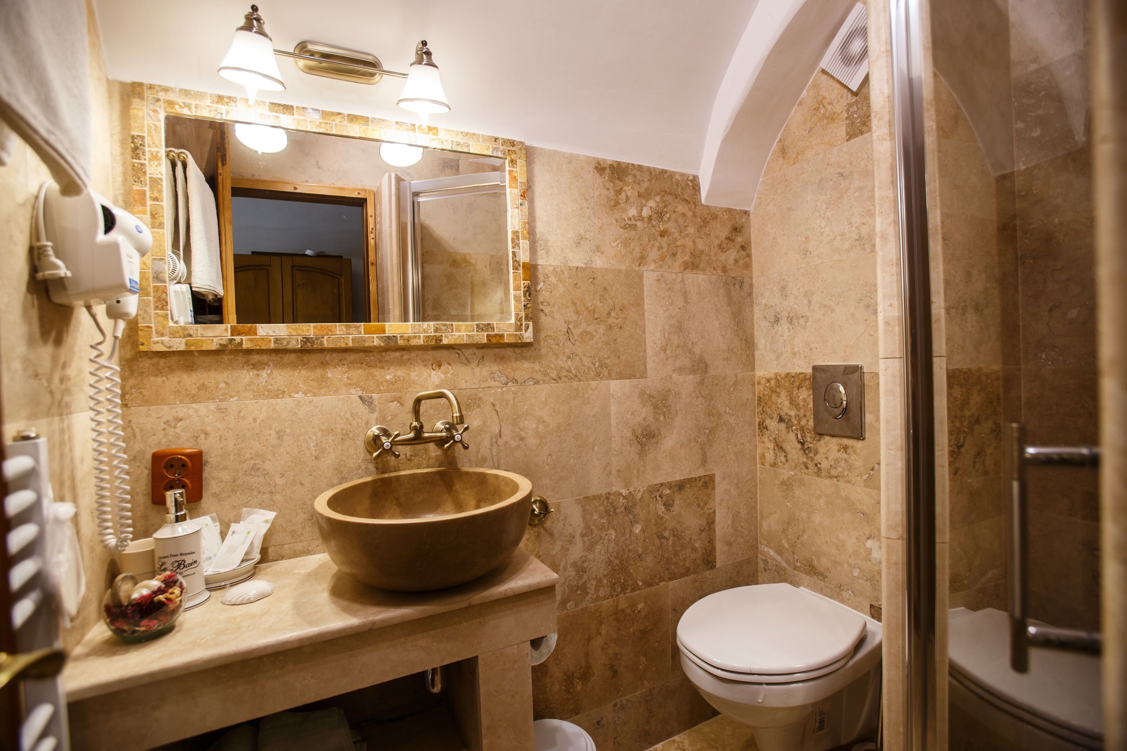A bathroom with a beige marble sink, a mirror with lights, a toilet, and a shower.