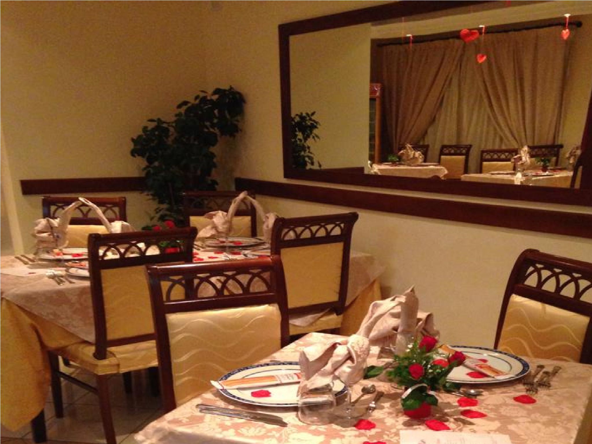 A dining area with a table set for four, chairs, a potted plant, and a mirror above the table.