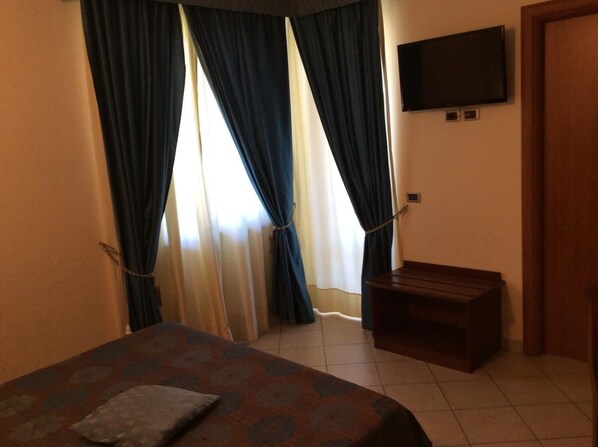 Habitación de hotel con una cama, un televisor montado en la pared y una pequeña mesa de madera.