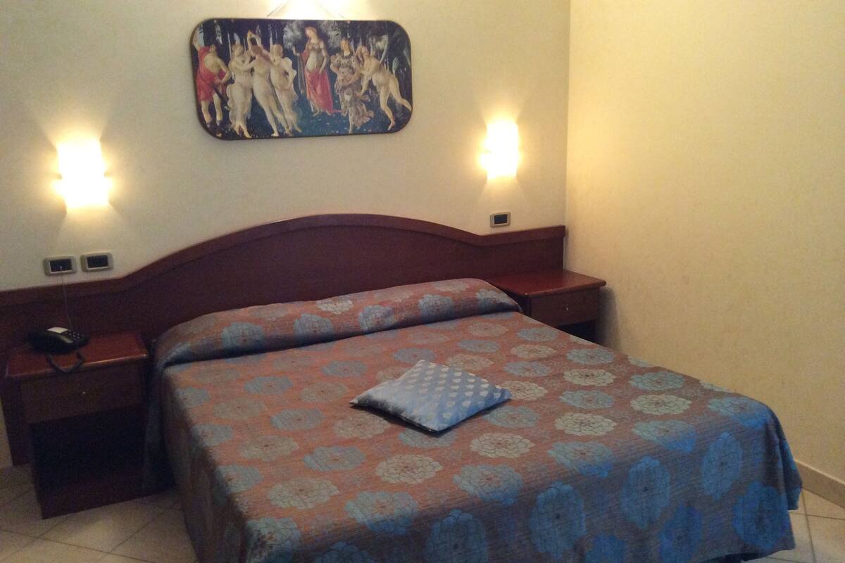 Une chambre à coucher avec un lit, des tables de chevet, un tableau au mur et deux lampes fixées au mur.