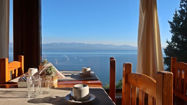A table set for two with a view of a calm sea and distant mountains. - Hosteria Ventus Patagonia (San Carlos de Bariloche)