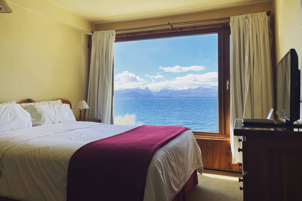 Ein Hotelzimmer mit großem Fenster und Blick auf ein Gewässer und Berge.