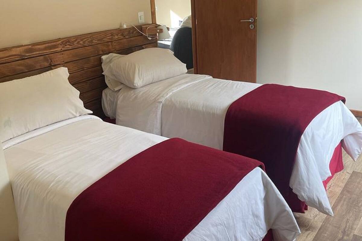 Ein Zimmer mit zwei Betten, jeweils mit weißer Bettwäsche und roten Akzenten, Holz-Kopfteilen und einem großen Spiegel an der Wand.