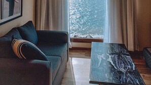 A living room with a sofa, a coffee table, and a view of a body of water through a window. - Hosteria Ventus Patagonia (San Carlos de Bariloche)