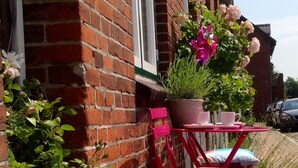 A red brick building with a window, a red folding chair, and a potted plant with pink flowers. - LOFTvorSYLT (Friedrichstadt)