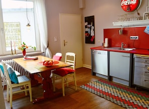 A compact kitchen with a red countertop, a dishwasher, and a dining area with a wooden table and chairs.