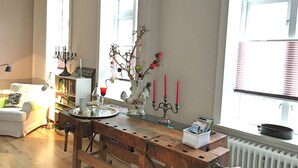A cozy living room with a wooden dining table, a bookshelf, and a window with blinds. - LOFTvorSYLT (Friedrichstadt)