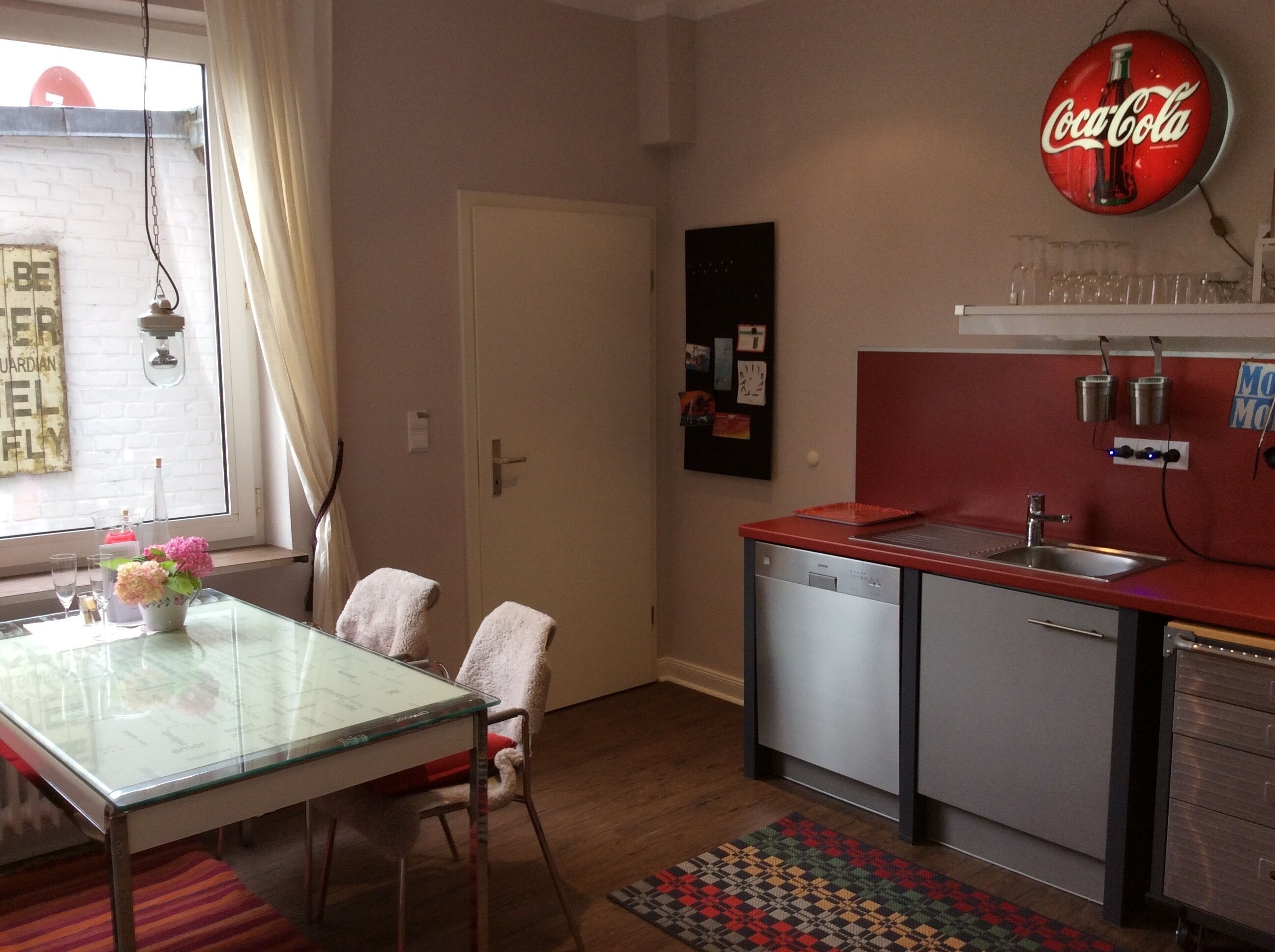 A compact kitchen with a red countertop, a dishwasher, and a Coca-Cola sign.