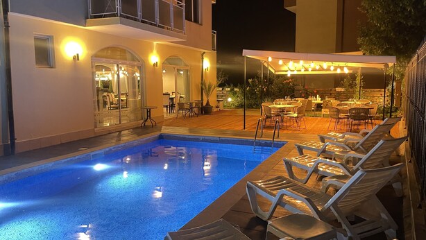 Piscina com espreguiçadeiras e zona de refeições ao ar livre à noite.