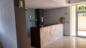 Uma área de recepção com balcão de pedra, um relógio e uma planta na parede.