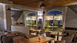 Interior de restaurante com mesas e cadeiras de madeira, grandes janelas e vista para o exterior.