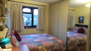 A bedroom with two beds, a window with curtains, a radiator, and a mirror. - The Cedars House B&B (Nuneaton)