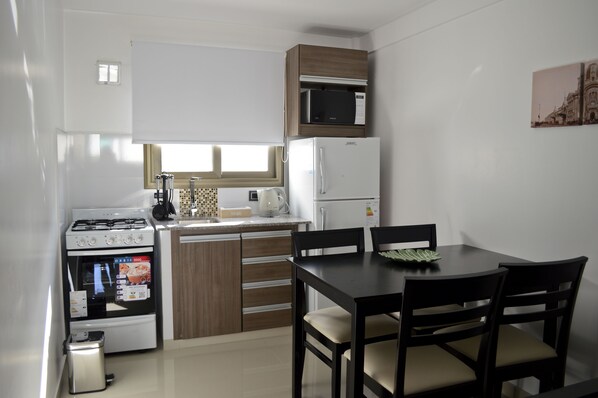 Cocina compacta con estufa, microondas y refrigerador. Hay una mesa de comedor con sillas y una ventana sobre el lavadero.