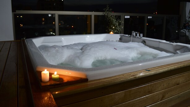 Un bain à remous avec des bougies, installé sur une terrasse en bois, offrant une vue sur le paysage urbain illuminé la nuit.