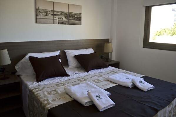 A neatly made bed with a patterned bedspread, two pillows, and folded towels on a dark-colored mattress.