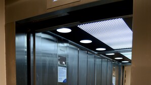 L’intérieur d’un ascenseur, avec des parois métalliques, un panneau de commande et une barre d’appui.