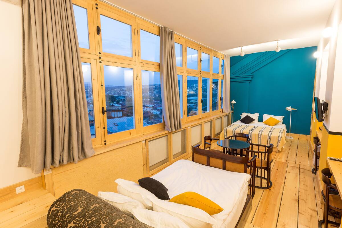 A room with large windows, a bed, a desk, and a chair.