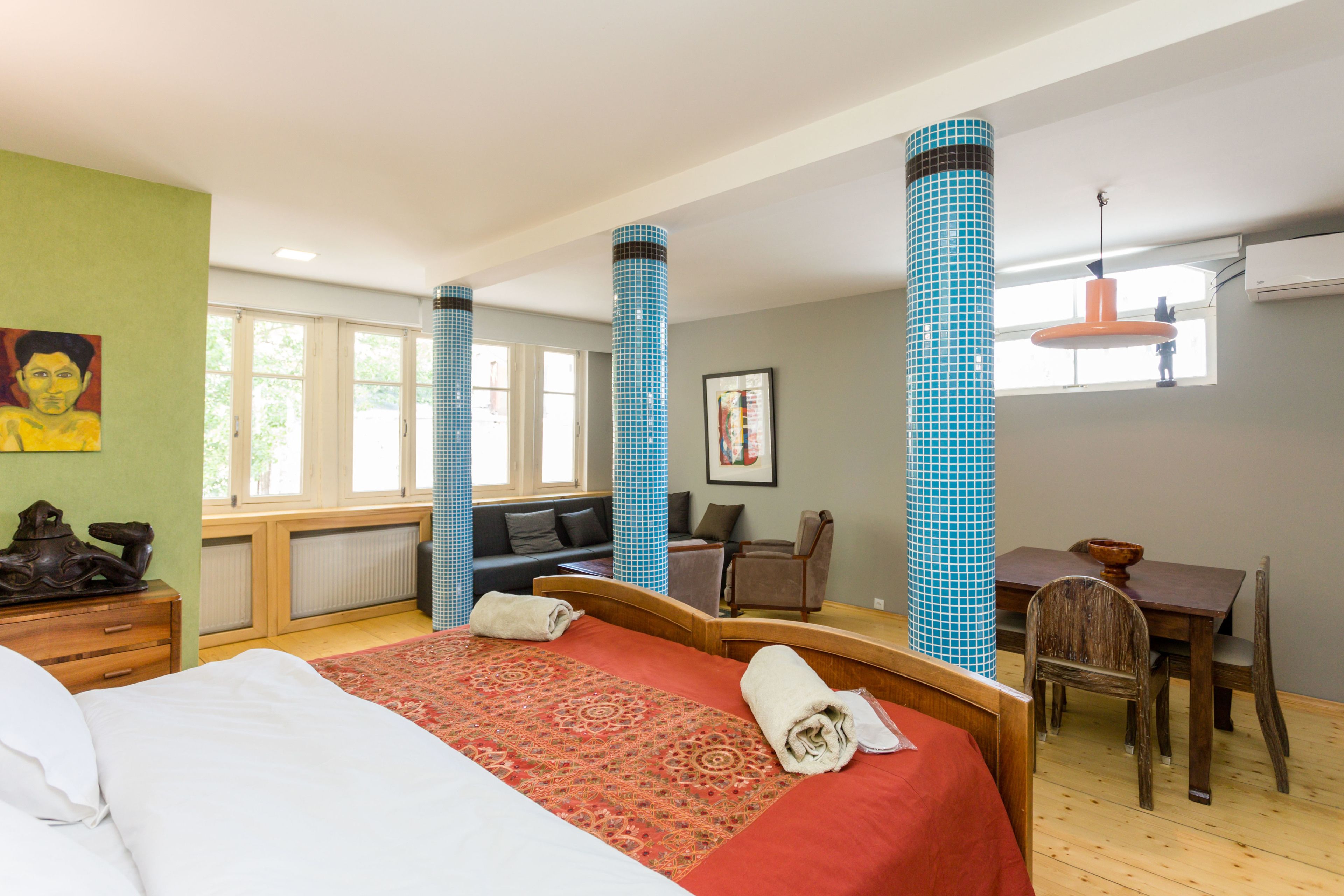 A hotel room with a large bed, a wooden desk, a chair, a sofa, and a window with a view.