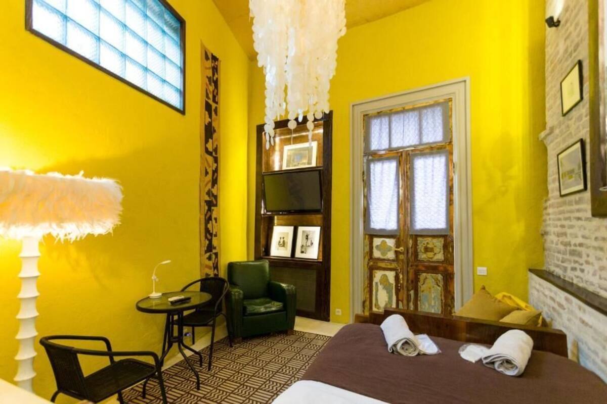 A hotel room with a bed, a chair, a small table, a lamp, and a television.