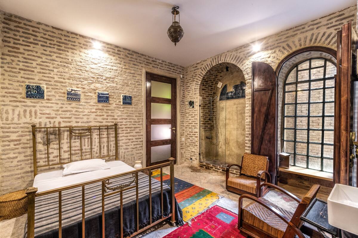 A room with a bed, a chair, a window, and a door.