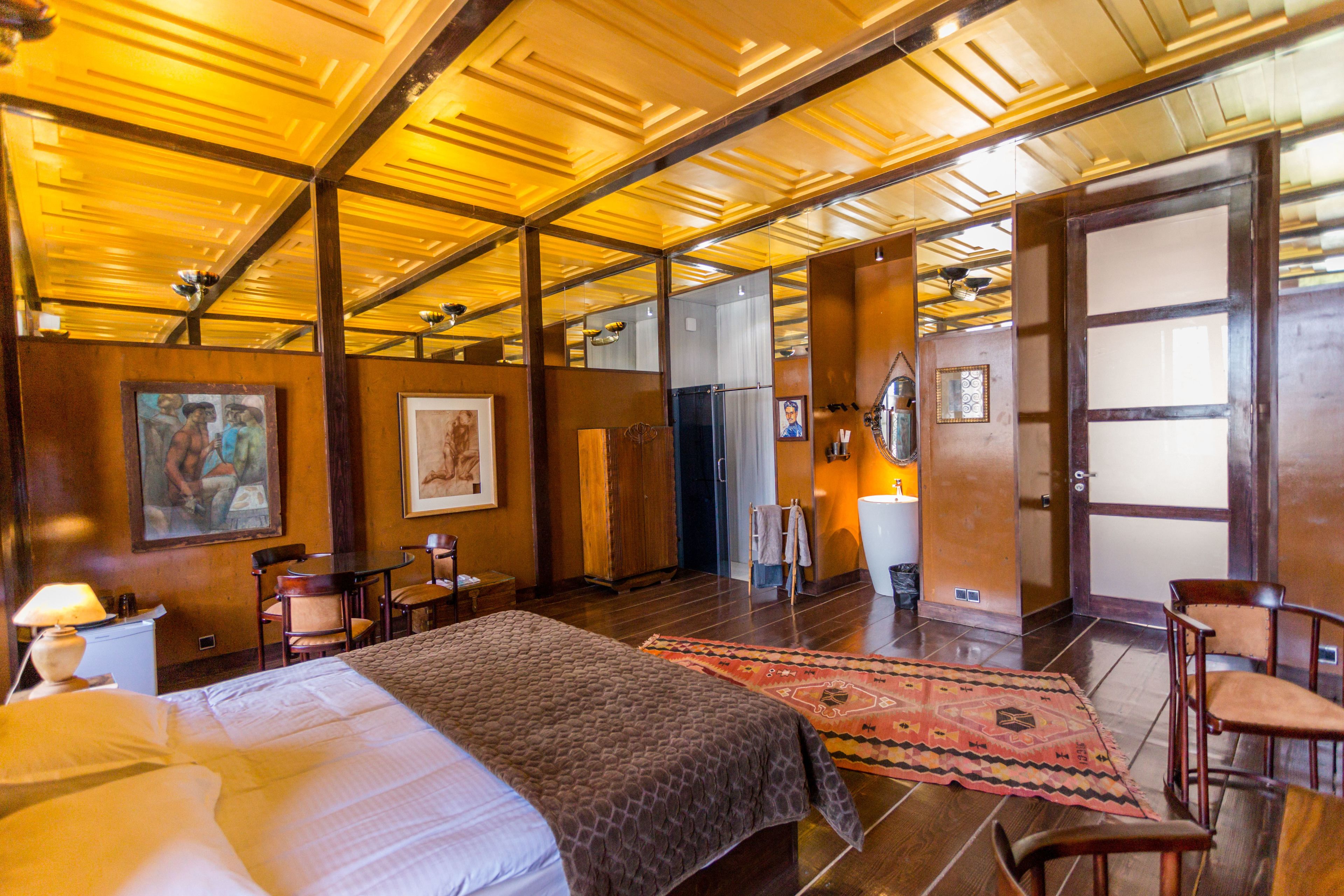A hotel room with a large bed, wooden ceiling, and a small sitting area with chairs and a table.