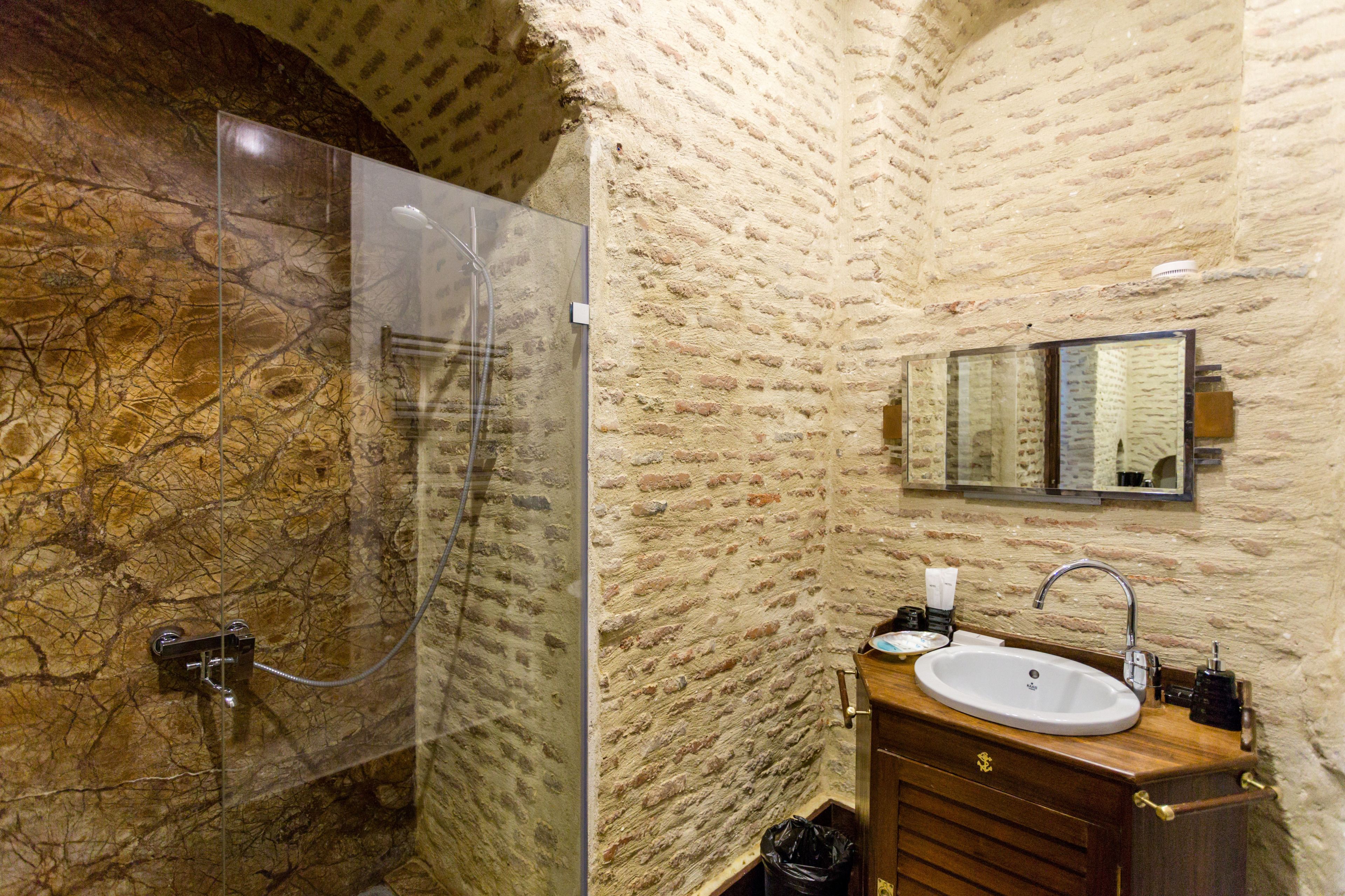 A bathroom with a stone wall, a glass shower enclosure, a wooden vanity with a sink, and a mirror above the vanity.