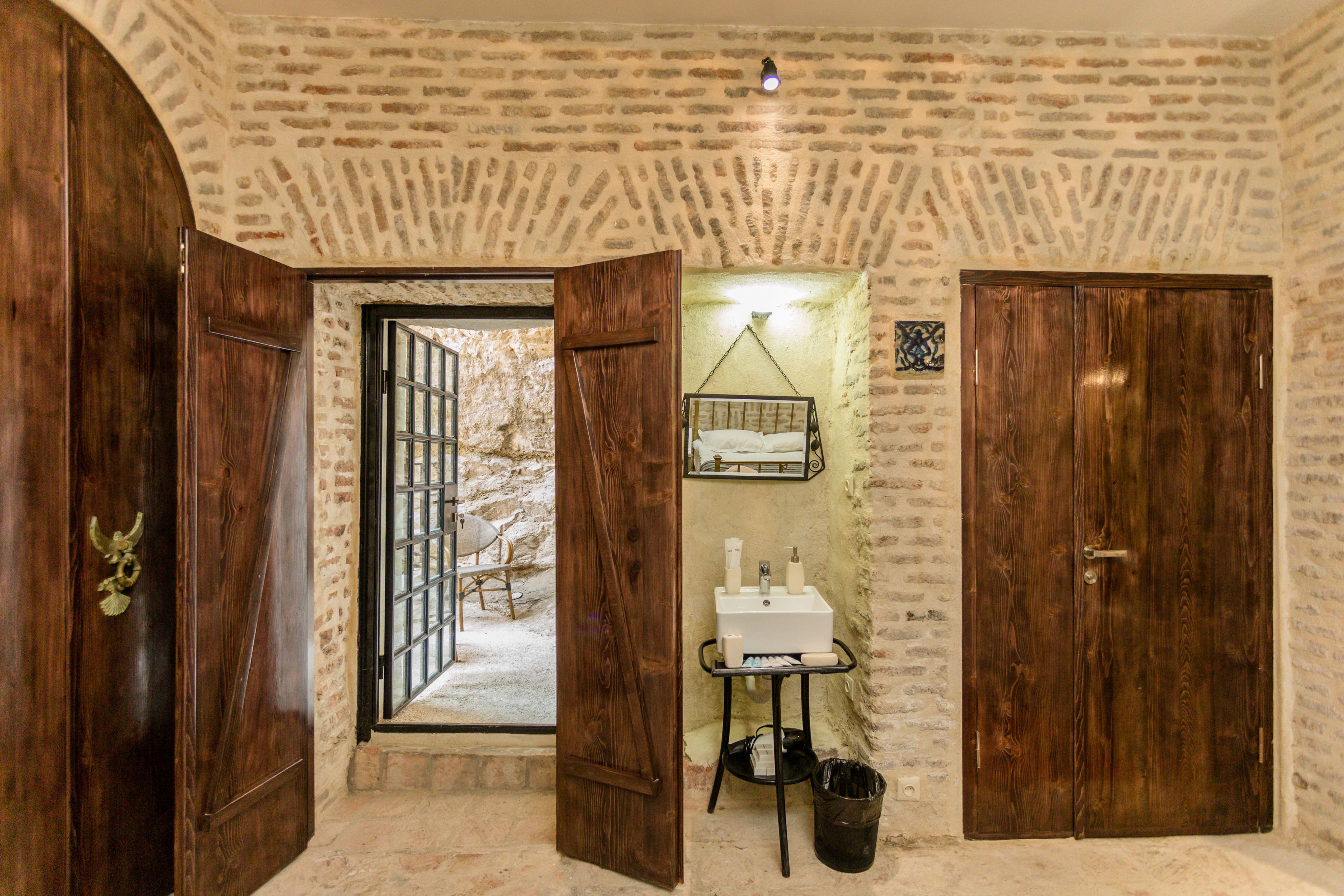 A rustic room with a stone wall, wooden doors, a small sink, and a hanging chair.