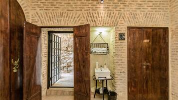 A rustic room with a stone wall, wooden doors, a small sink, and a hanging chair.