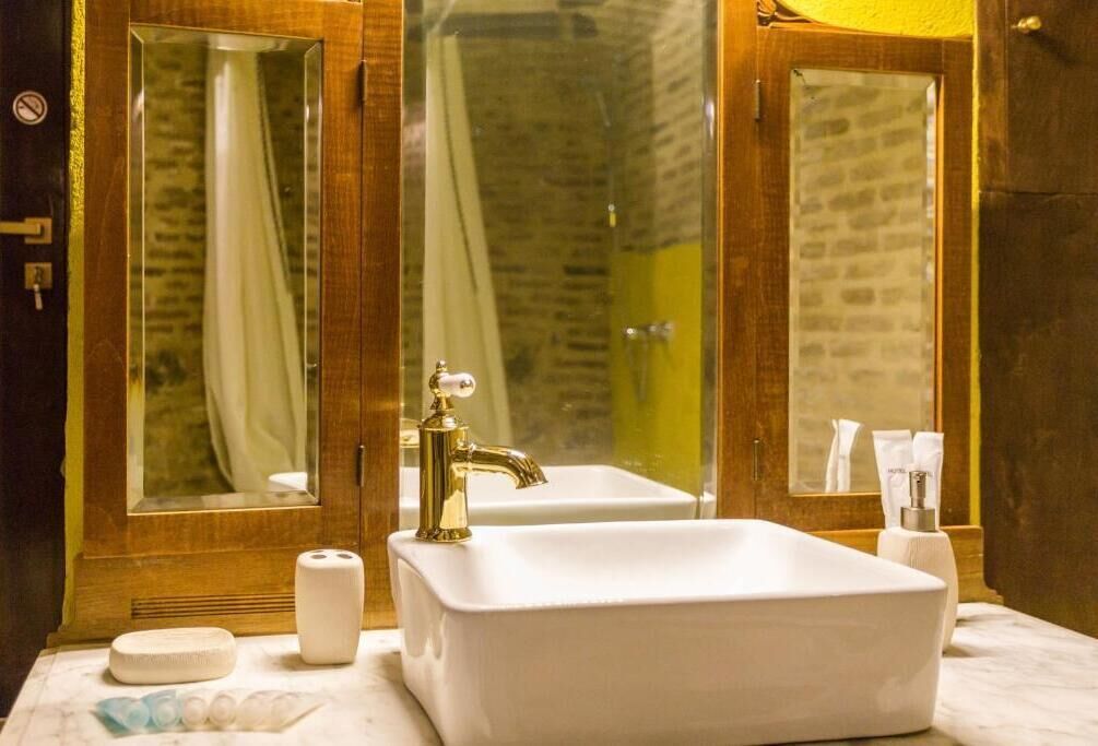 A bathroom with a white sink, a gold faucet, and two mirrors.