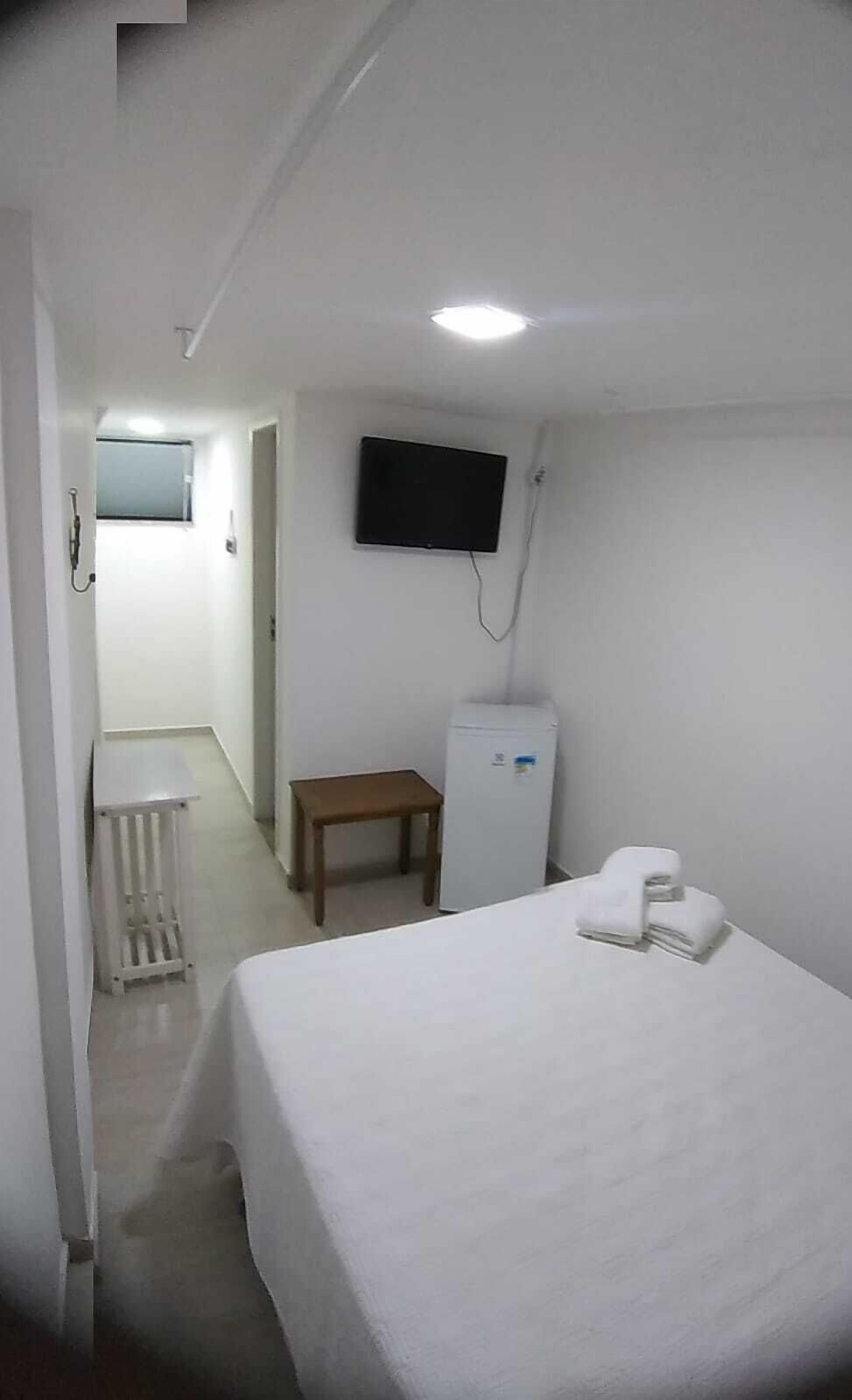 Una habitación de hotel con cama, una mesita, un refrigerador, un televisor y un radiador.