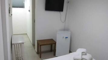 Una habitación de hotel con cama, una mesita, un refrigerador, un televisor y un radiador.