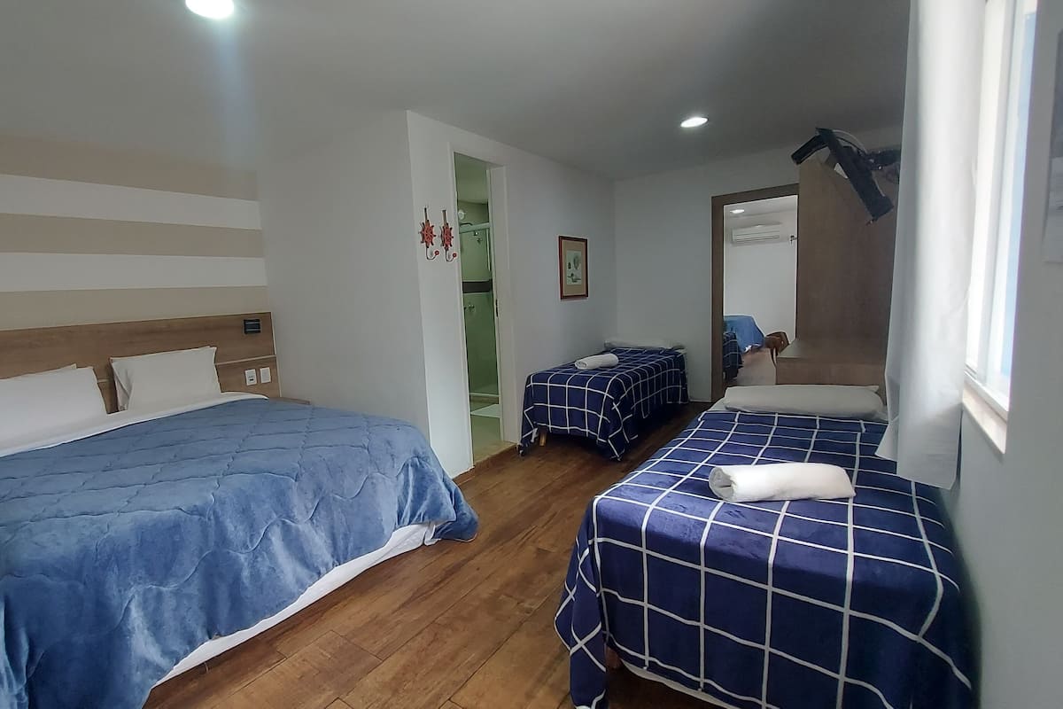 A hotel room with two beds, a wooden floor, a shower area, and a window with curtains.
