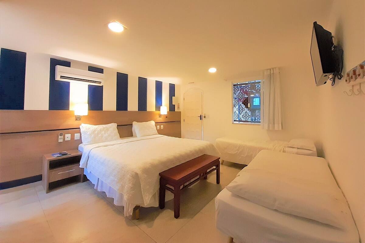 A hotel room with a large bed, a smaller bed, a bench, a nightstand, and a TV mounted on the wall.