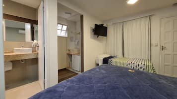 A bedroom with a bed, a bedside table, a flat-screen TV mounted on the wall, and a window with curtains.