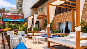 A poolside area with wooden loungers, a stone wall, and a sign for 'Pousada da Praia.' - Pousada da Prainha (Arraial do Cabo)