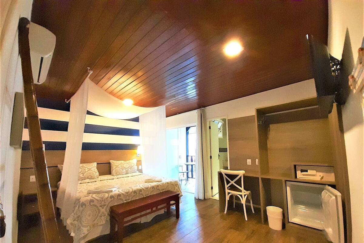 A bedroom with a bed, bedside table, bench, and a small desk with a chair.