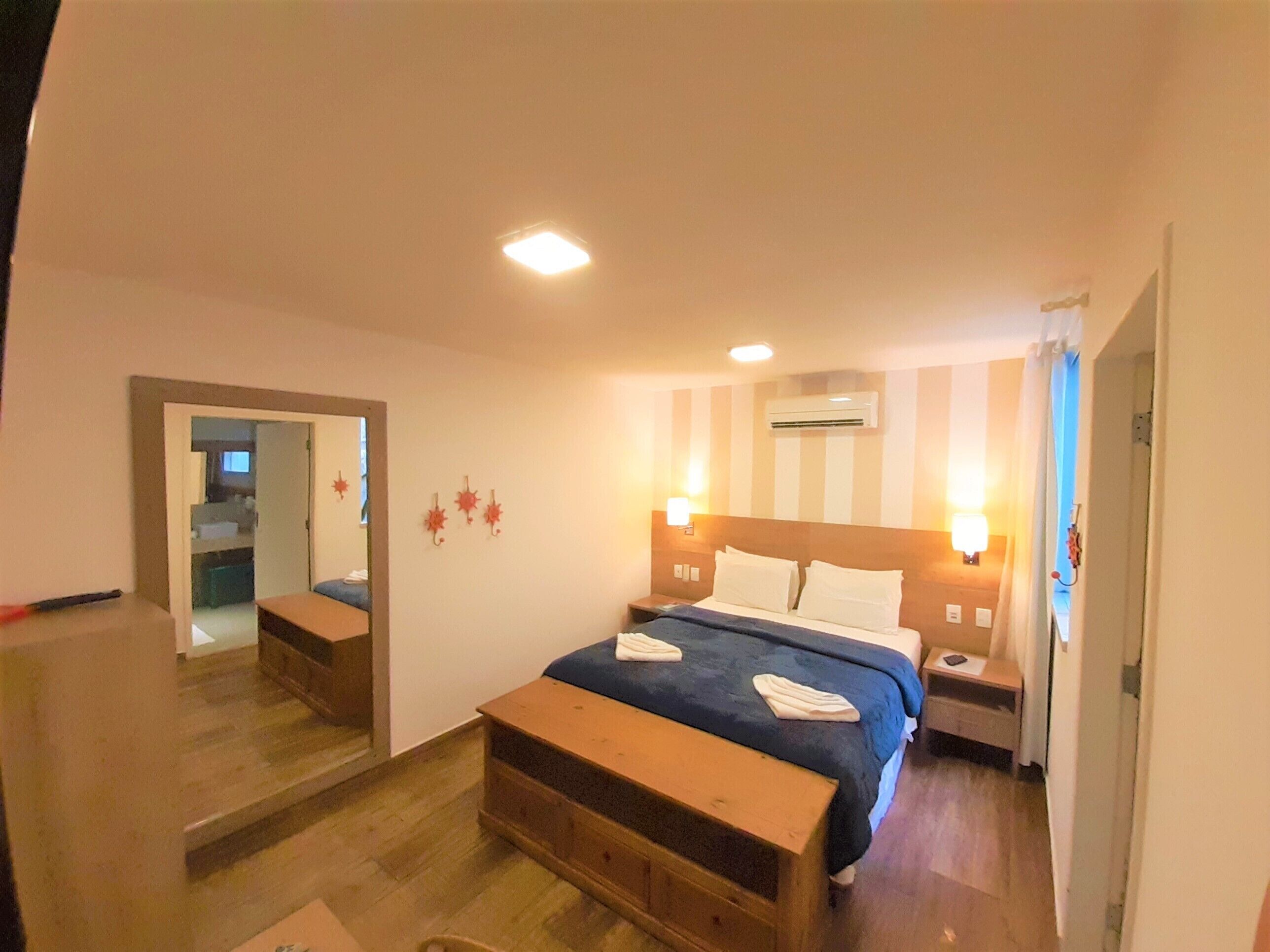 A hotel room with a bed, bedside tables, a mirror, and a wooden bench.