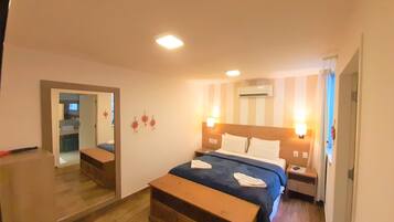 A hotel room with a bed, bedside tables, a mirror, and a wooden bench.