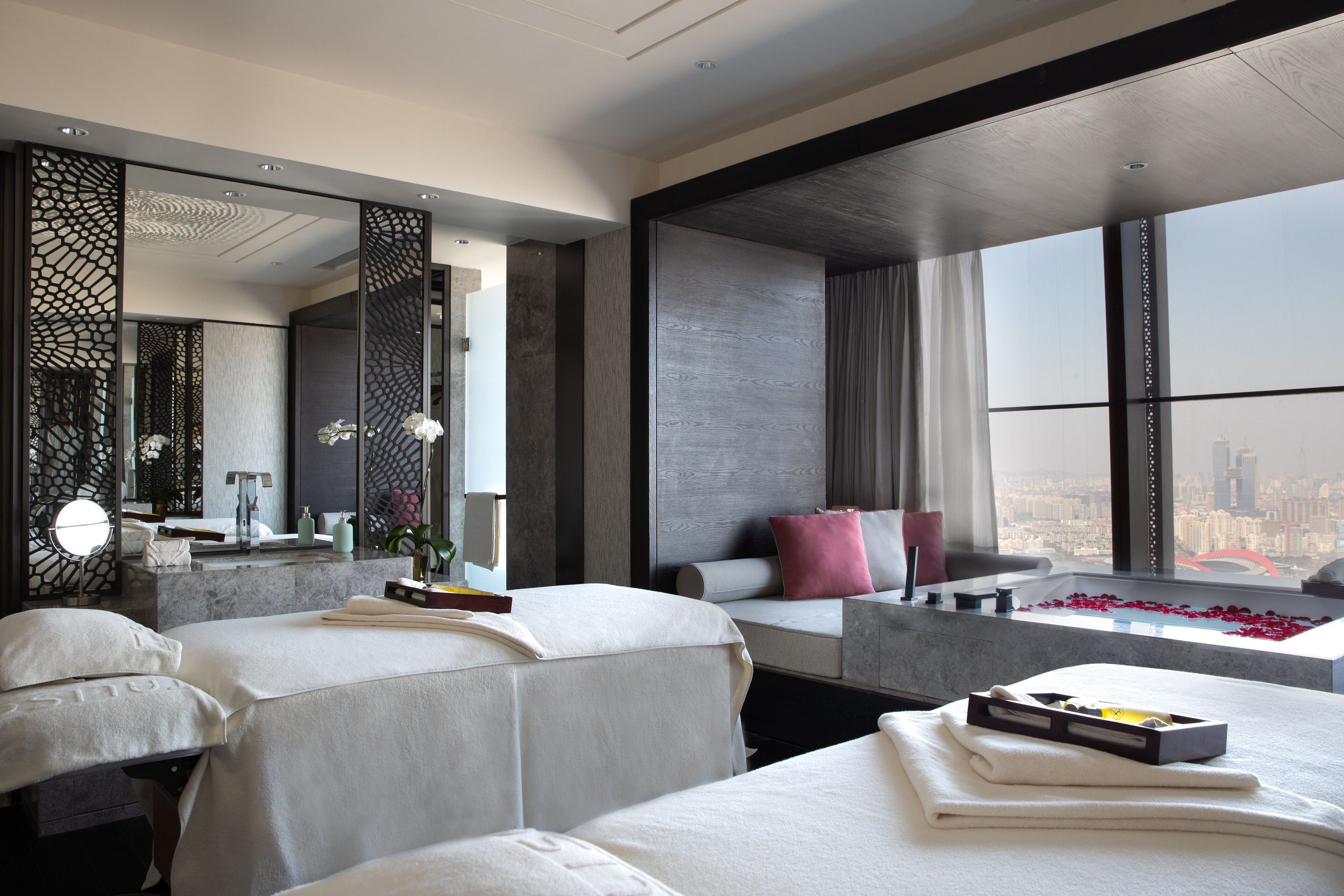 A modern hotel room with two beds, a large mirror, a bathtub with rose petals, and a city view.