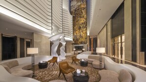 Eine moderne Lobby mit einer zentralen Sitzecke, einer großen Wand mit vertikalem Design und einer hohen Decke mit linearer Beleuchtung.