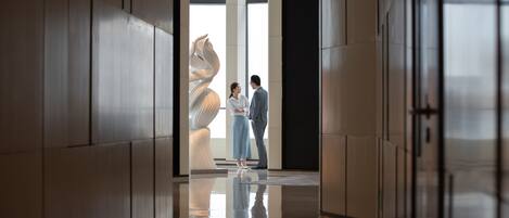 A modern interior with a reflective floor, a large abstract sculpture, and a couple standing in the center.