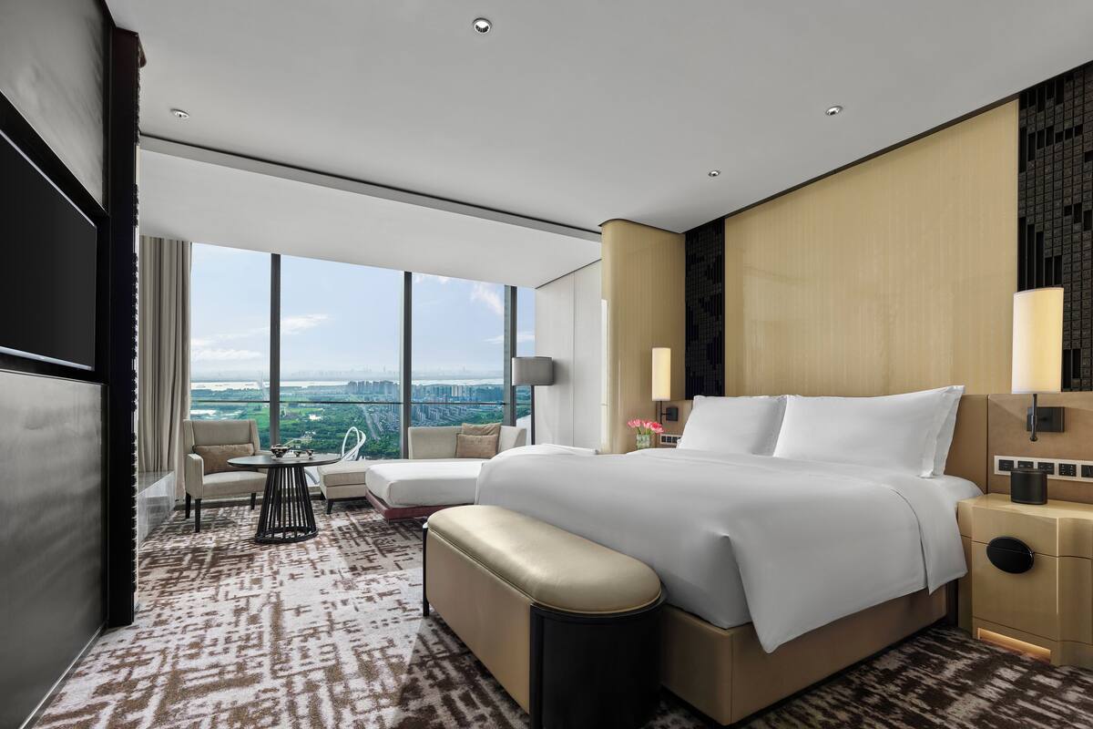 Una habitación de hotel moderna con una cama grande, un escritorio y vistas a un paisaje urbano.